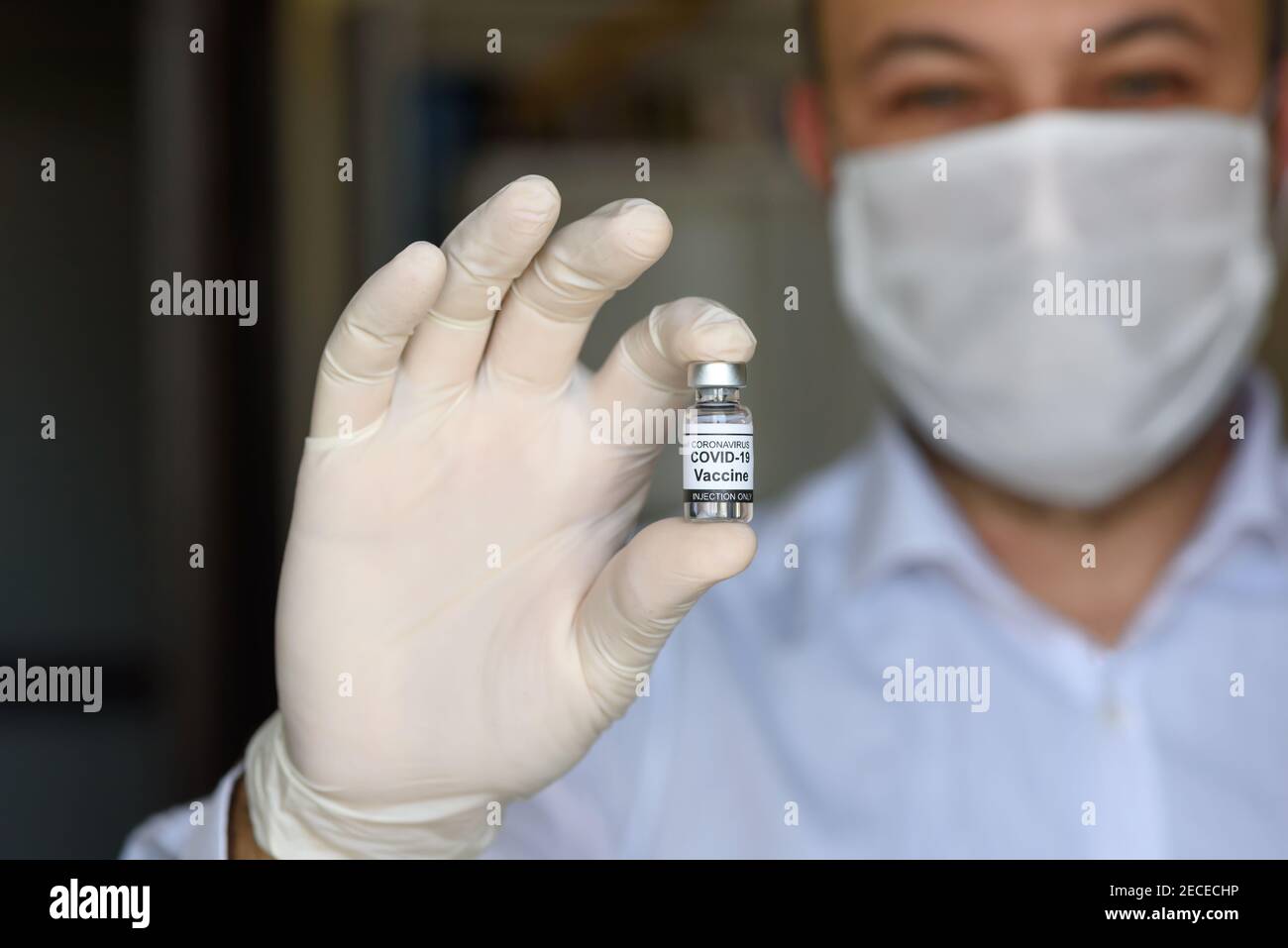 Il medico con guanti bianchi contiene un flacone con vaccino COVID-19. Concetto di medicina, sperimentazione clinica e trattamento dovuto al coronavirus SARS-COV-2. Sfocatura Foto Stock