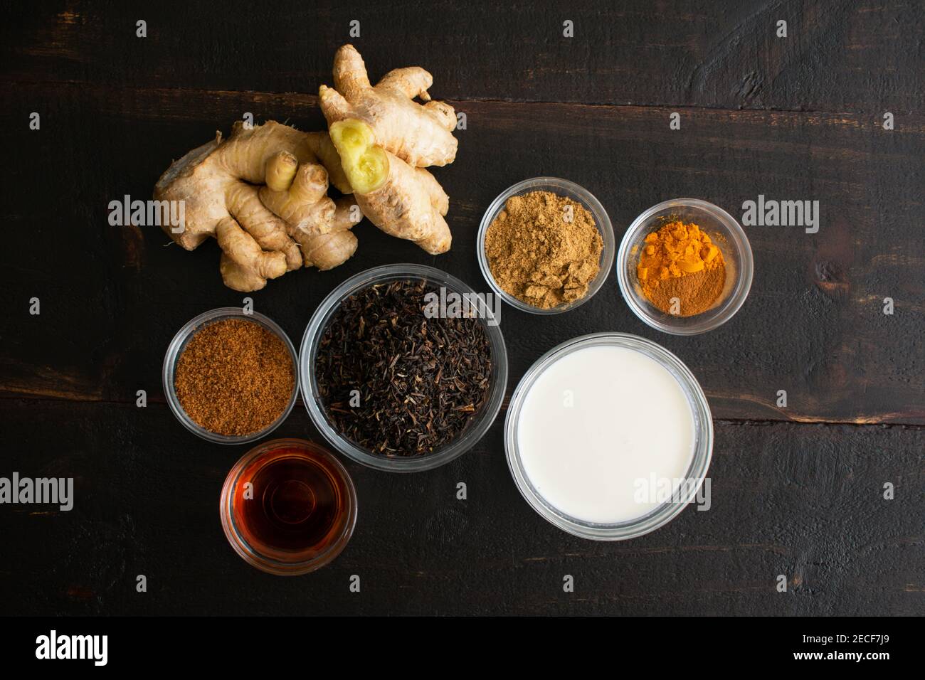 Cardamomo cannella curcuma tè freddo ingredienti su un legno scuro sfondo: Foglie di tè sciolto, zucchero di palma di cocco, sciroppo d'acero, latte di cocco, zenzero Foto Stock