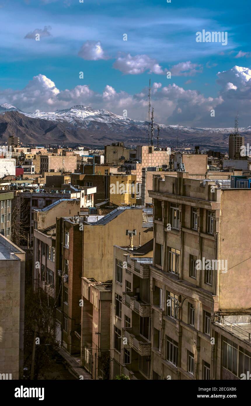 Vista dei tetti di Teheran densamente popolato contro cielo blu con nuvole e montagne innevate Foto Stock