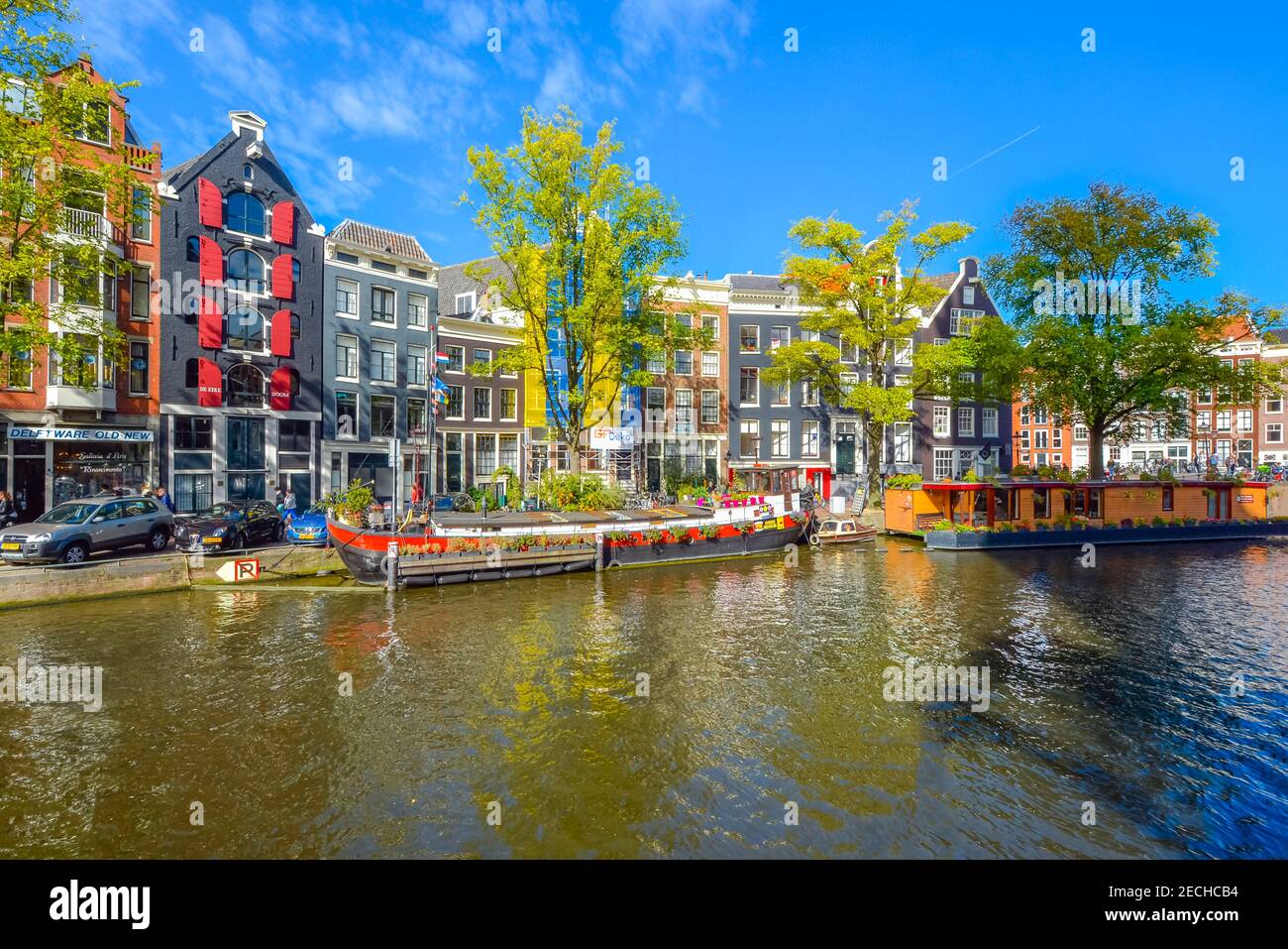 Le case galleggianti colorate costeggiano il canale di fronte alle case olandesi colorate in una giornata di sole all'inizio dell'autunno ad Amsterdam, Paesi Bassi Foto Stock