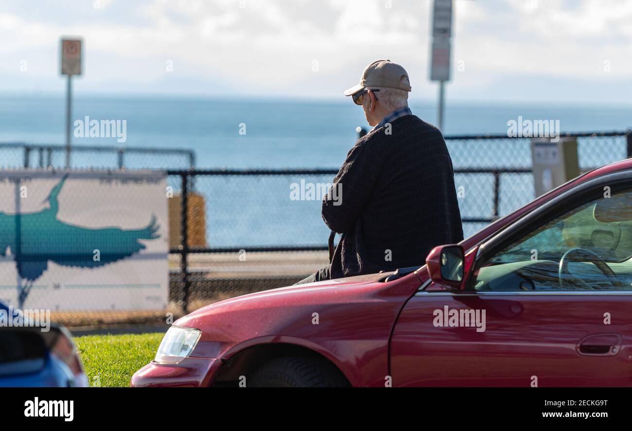 Vista posteriore di un uomo anziano seduto su un tronco della macchina godendo la vista del mare. White Rock, British Columbia, Canada. Vista sulla strada, foto di viaggio, selettiva Foto Stock