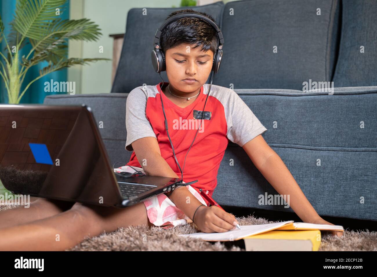 bambino con cuffie che annotano fino a prenotare dal laptop durante la lezione virtuale dal laptop a casa - concetto di classe online, formazione online Foto Stock