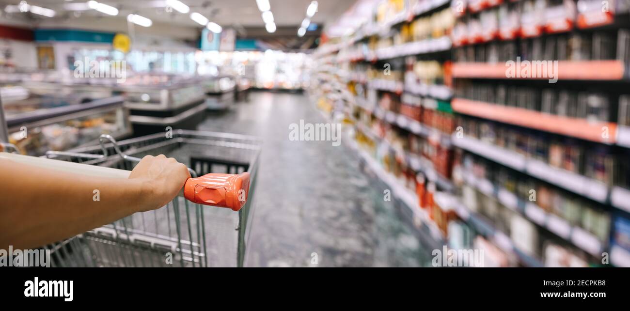 Primo piano di donna con il carrello della spesa al negozio di alimentari. Donna che spinge il carrello nel supermercato. Foto Stock