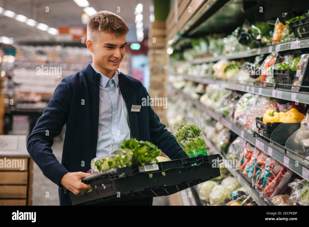 Assistente di negozio nel supermercato riapprovvigionamento verdure fresche in scaffali della sezione prodotti. Foto Stock