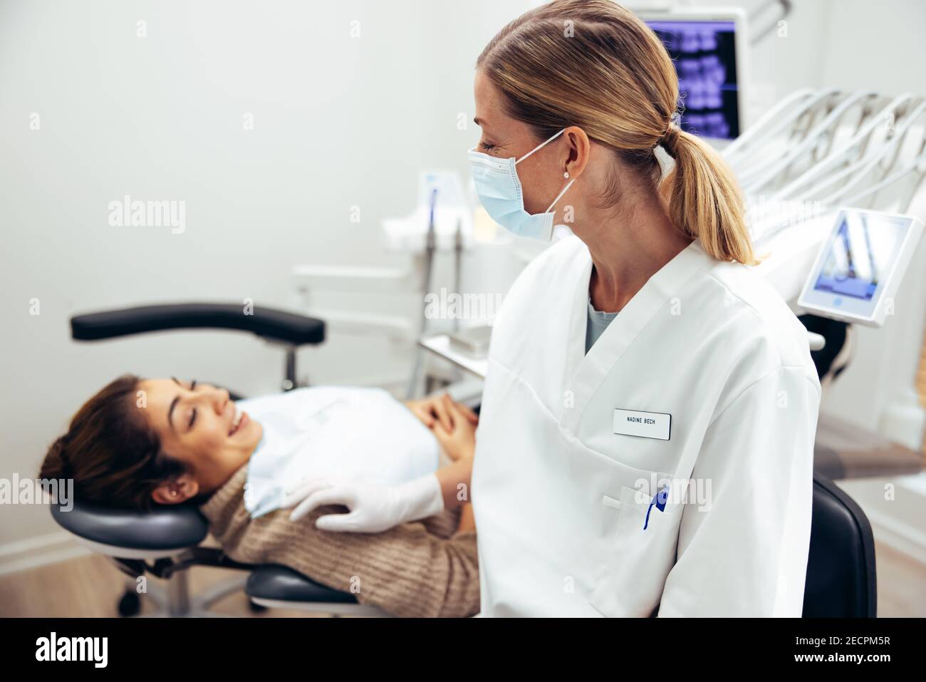 Dentista femminile che indossa la maschera facciale che parla con il paziente nella sedia del dentista. Medico dentale con paziente femminile in visita per controllo di routine. Foto Stock