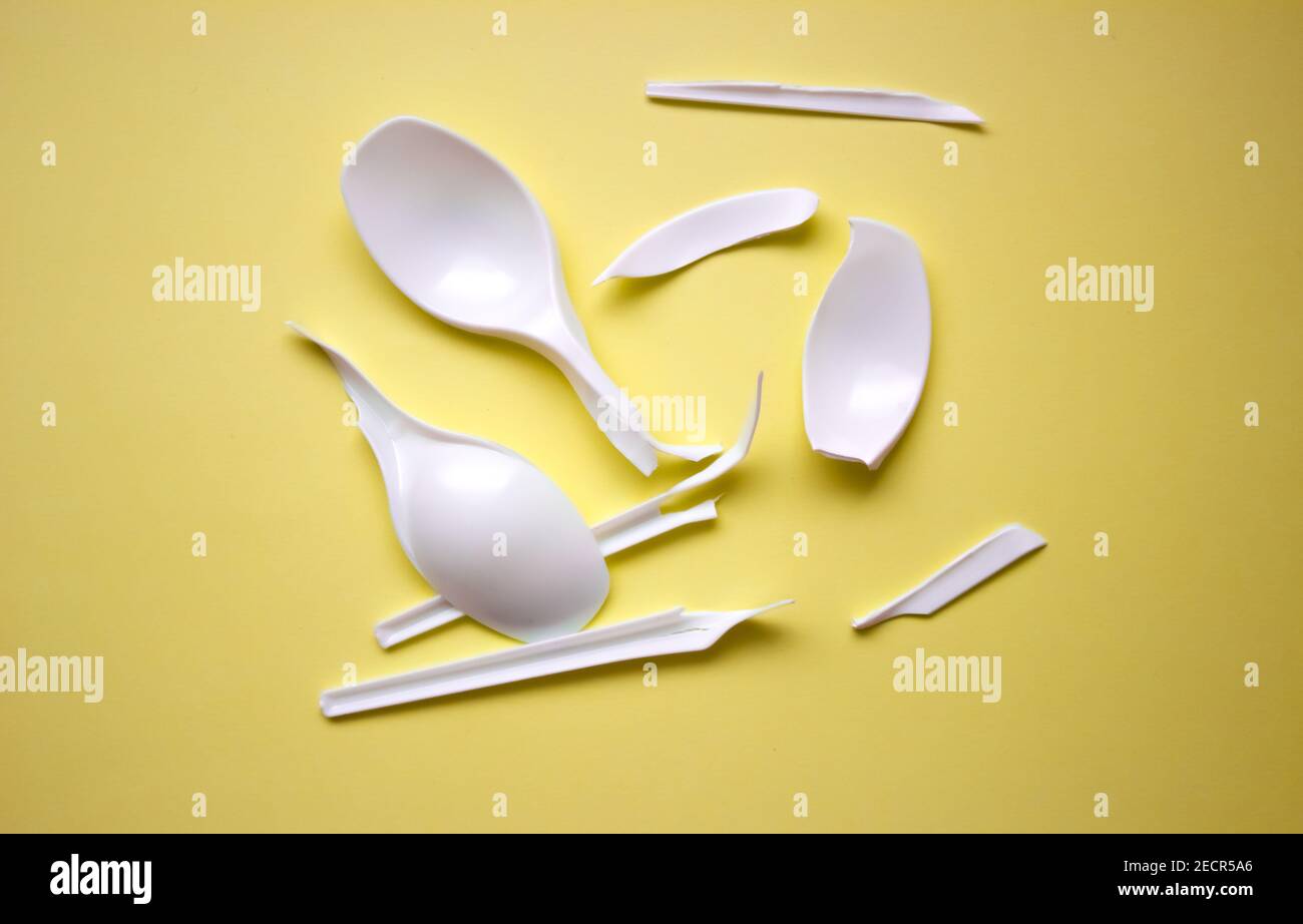 Cucchiai in plastica bianca monouso rotti. Plastica rotta su sfondo giallo. Posate monouso. Foto Stock