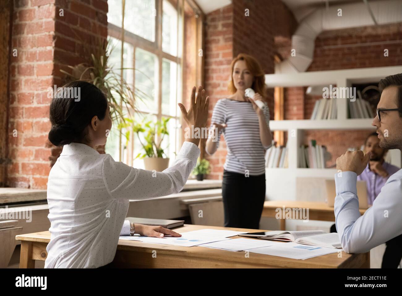 La donna etnica alza la mano alla riunione di ufficio Foto Stock