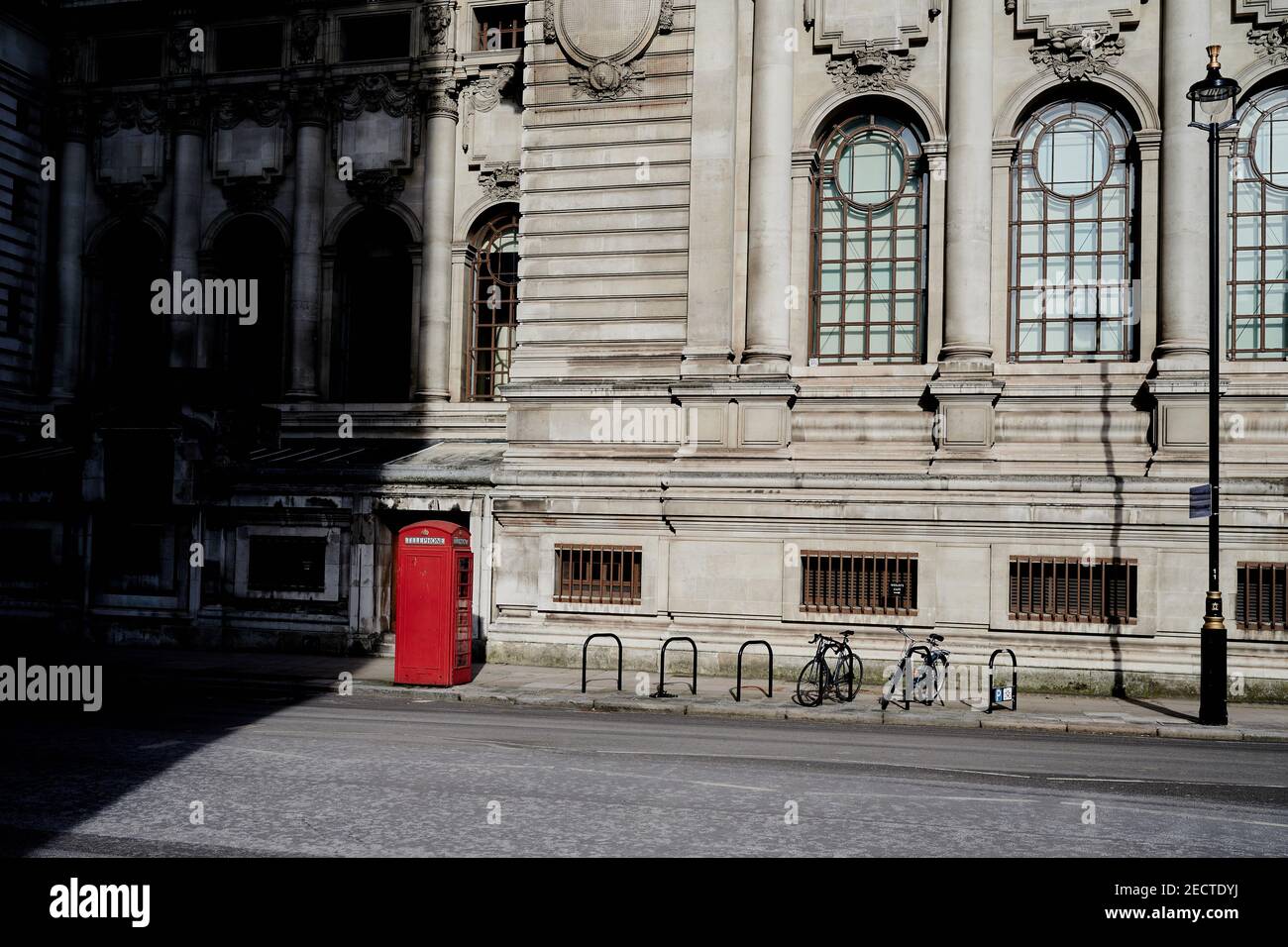 Londra UK - 13 Feb 2021: Scena vuota della strada londinese con box telefonico rosso e londs ombre in sole invernale di fronte al vecchio edificio del XIX secolo Foto Stock