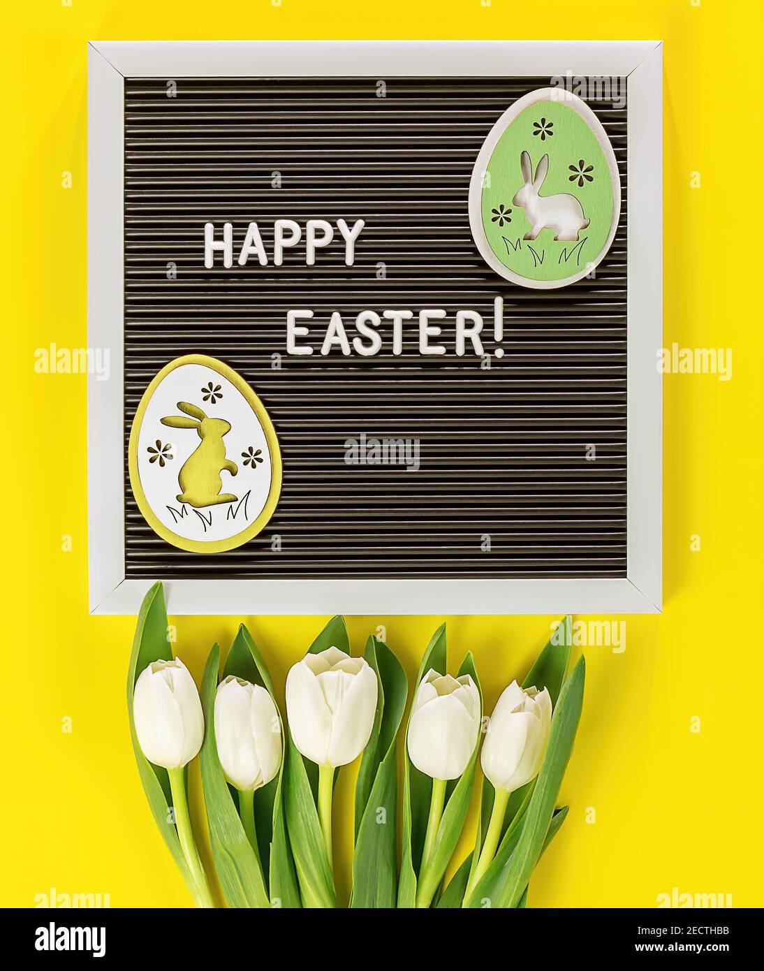 Uova di coniglio di Pasqua, fiori su sfondo giallo. Spazio di copia, vista dall'alto. Piatto di concetto di celebrazione pasquale. Foto Stock