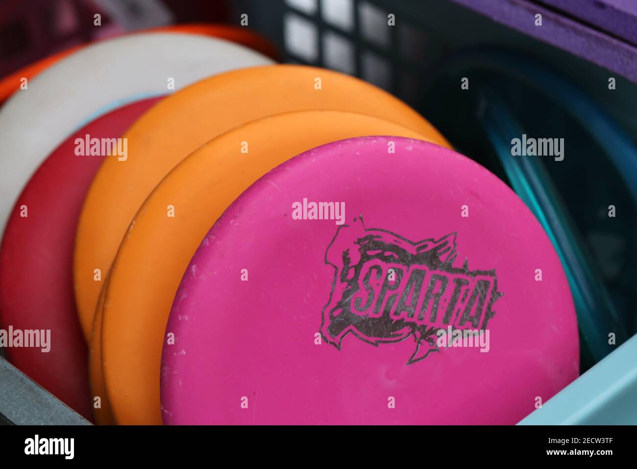 Molto colorato di dischi di golf frisbee in un cesto di plastica. Frisbee rosa, rosso, bianco e arancione. Uno di essi ha il logo Sparta. Editoriale di primo piano. Foto Stock
