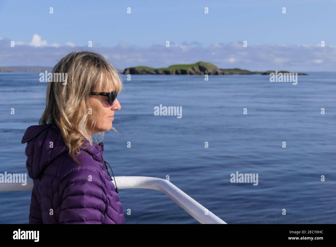 Una donna dai capelli biondi guarda fuori al mare da un Barca con occhiali da sole su un sole day.Sea e isola in sfondo Foto Stock