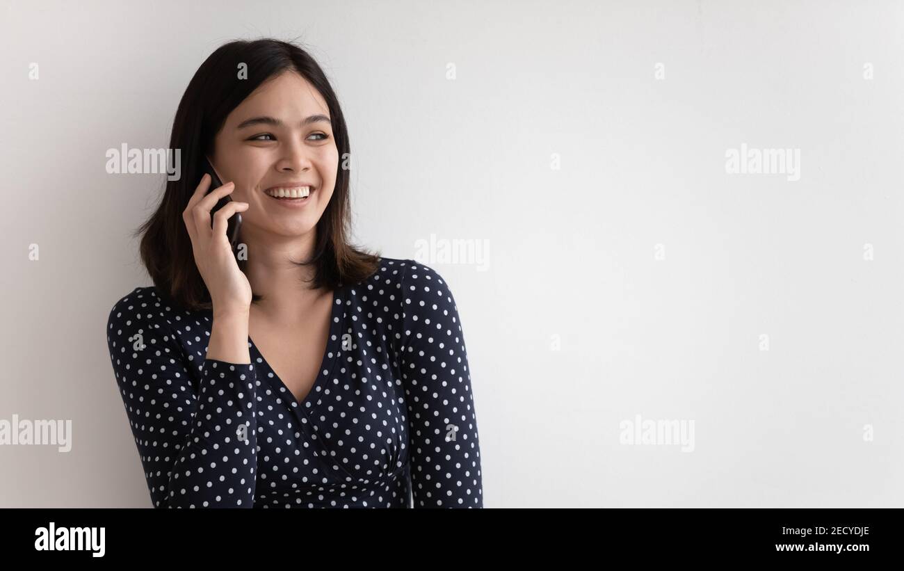 Molto gioiosa millennial asian femmina che chiacchiera tenendo il telefono cellulare all'orecchio Foto Stock