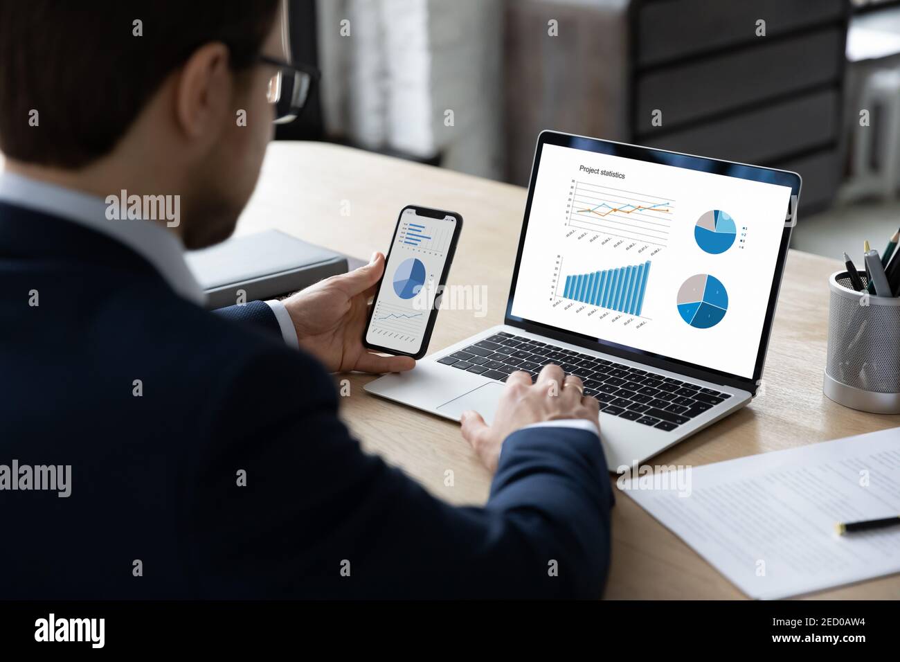 Vista posteriore del lavoro di un uomo d'affari su dispositivi con diagrammi finanziari Foto Stock