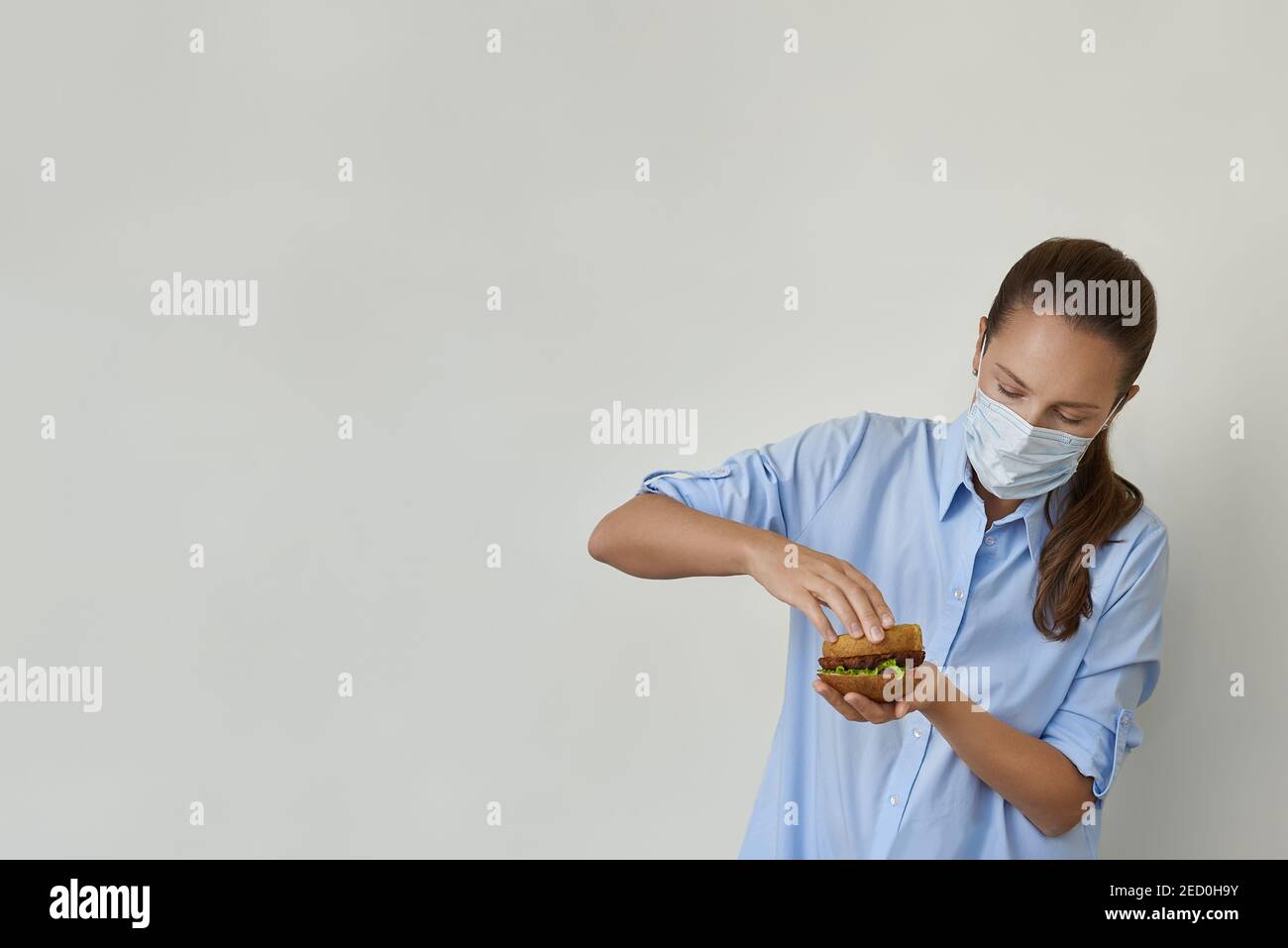 Bella giovane donna che cucinava hamburger vegano in maschera protettiva Foto Stock
