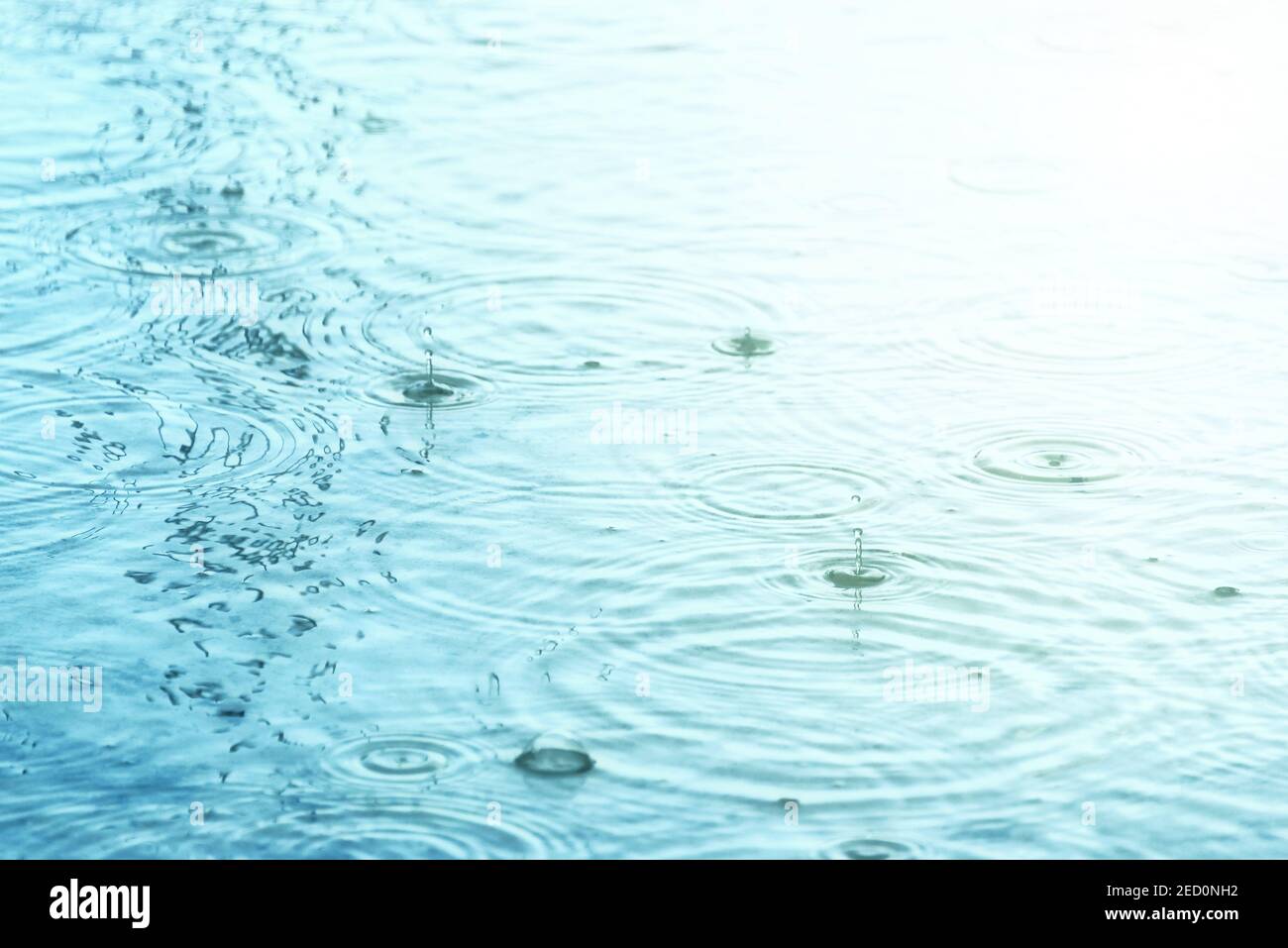 Gocce di pioggia che creano cerchi concentrici e goccioline sulla superficie dell'acqua Foto Stock