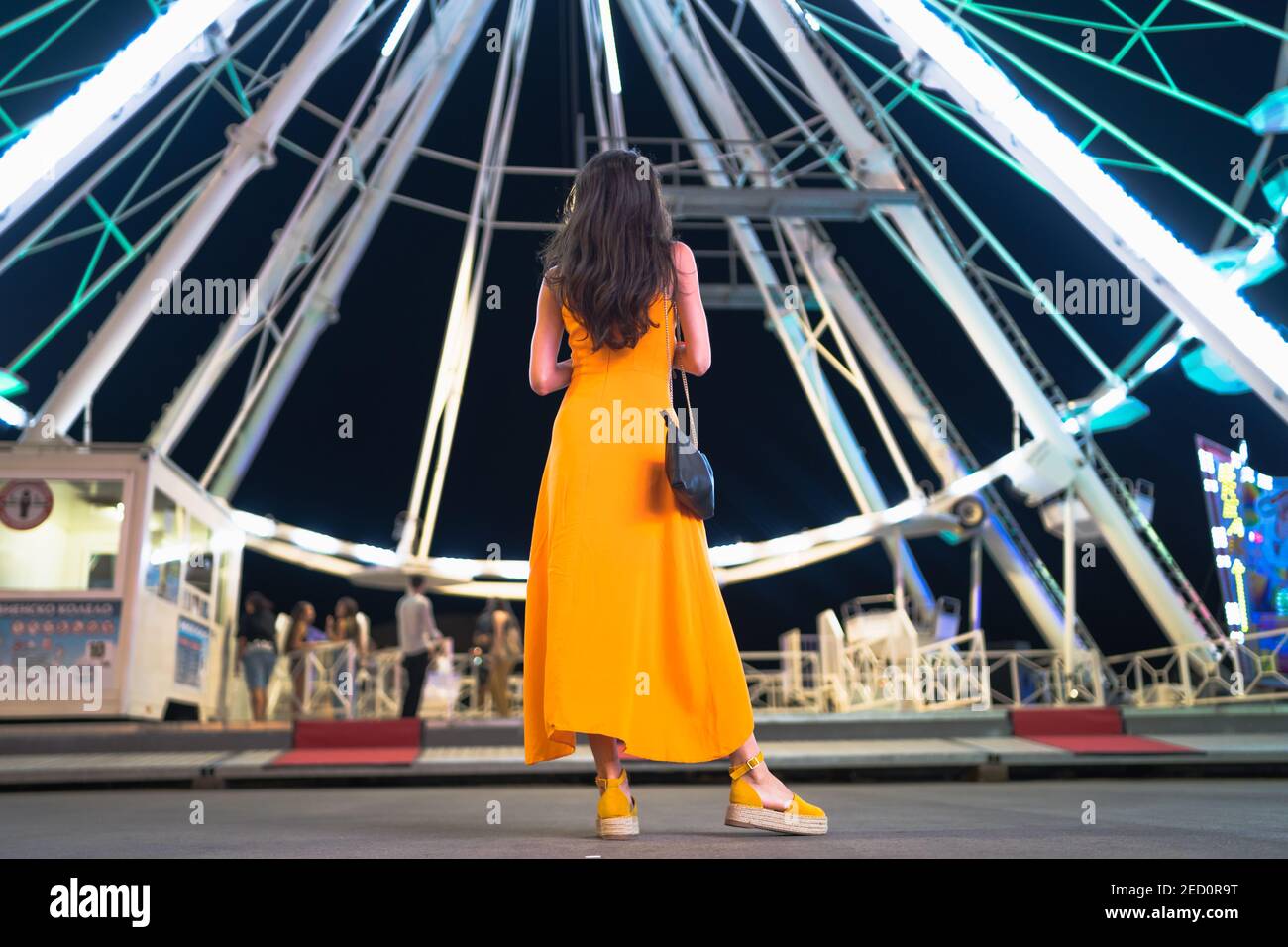Vista posteriore della donna vestita con abito arancione, in piedi davanti alla ruota panoramica Foto Stock