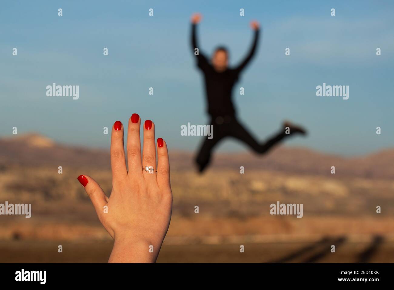 Proposta di matrimonio in Cappadocia, mano femminile con anello di fidanzamento e chiodi rossi, uomo saltante sfocato in background Foto Stock