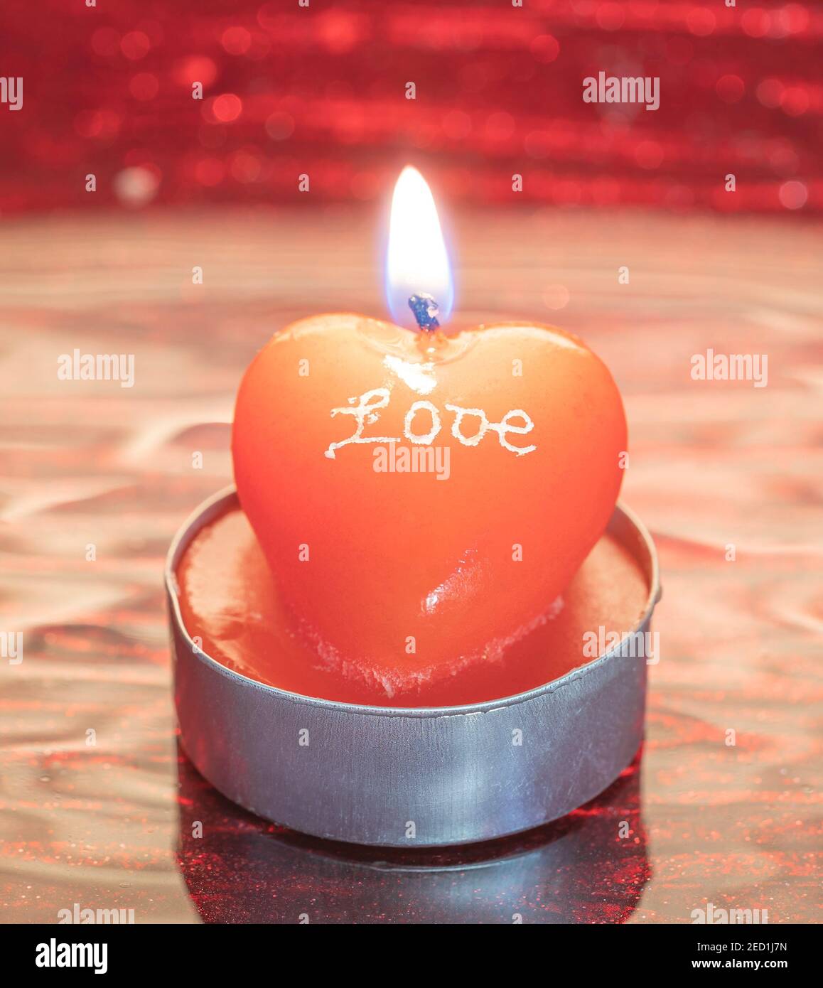 Una candela a forma di cuore con una fiamma e l'iscrizione AMORE su uno sfondo sfocato Foto Stock