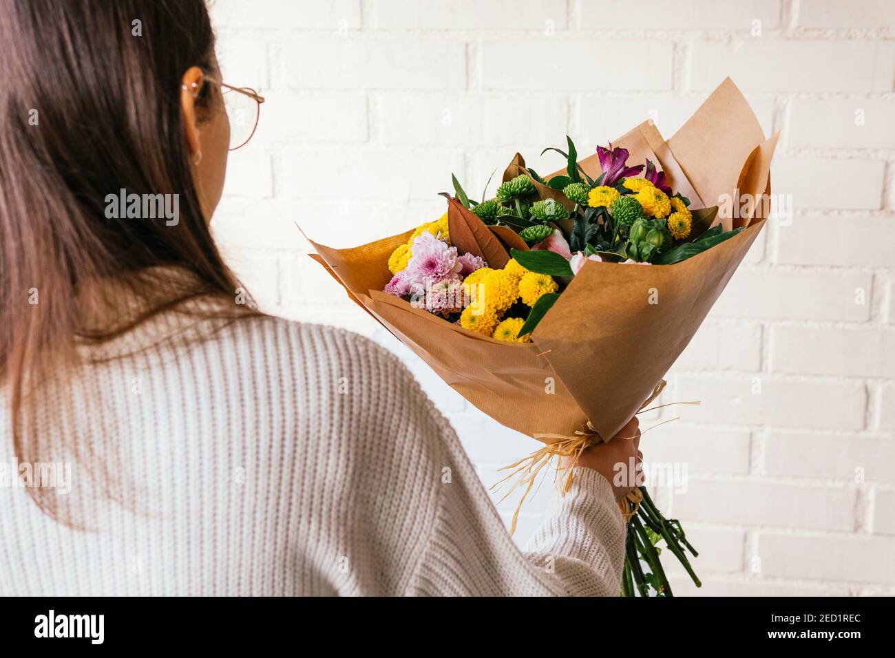 Crop persona irriconoscibile in piedi con mazzo di fiori freschi colorati sullo sfondo di muro di mattoni bianchi Foto Stock