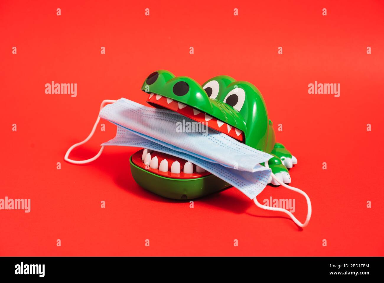 Giocattolo in plastica con denti a coccodrillo e maschera medica in denti su sfondo rosso in studio Foto Stock