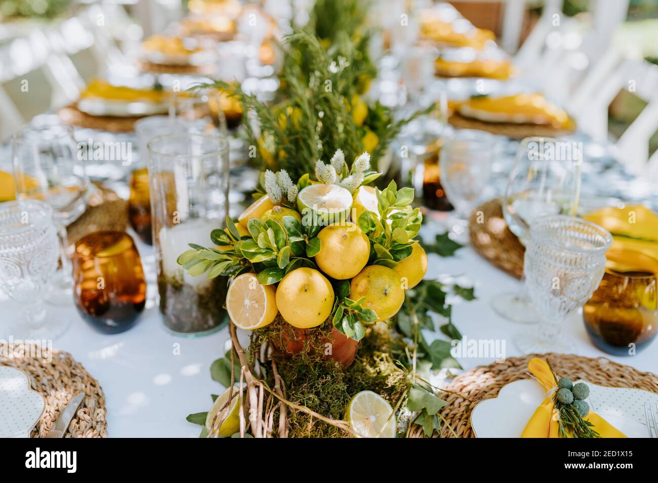 Tavolo lungo servito con bicchieri e piatti e decorato con composizioni di limone con piante Foto Stock