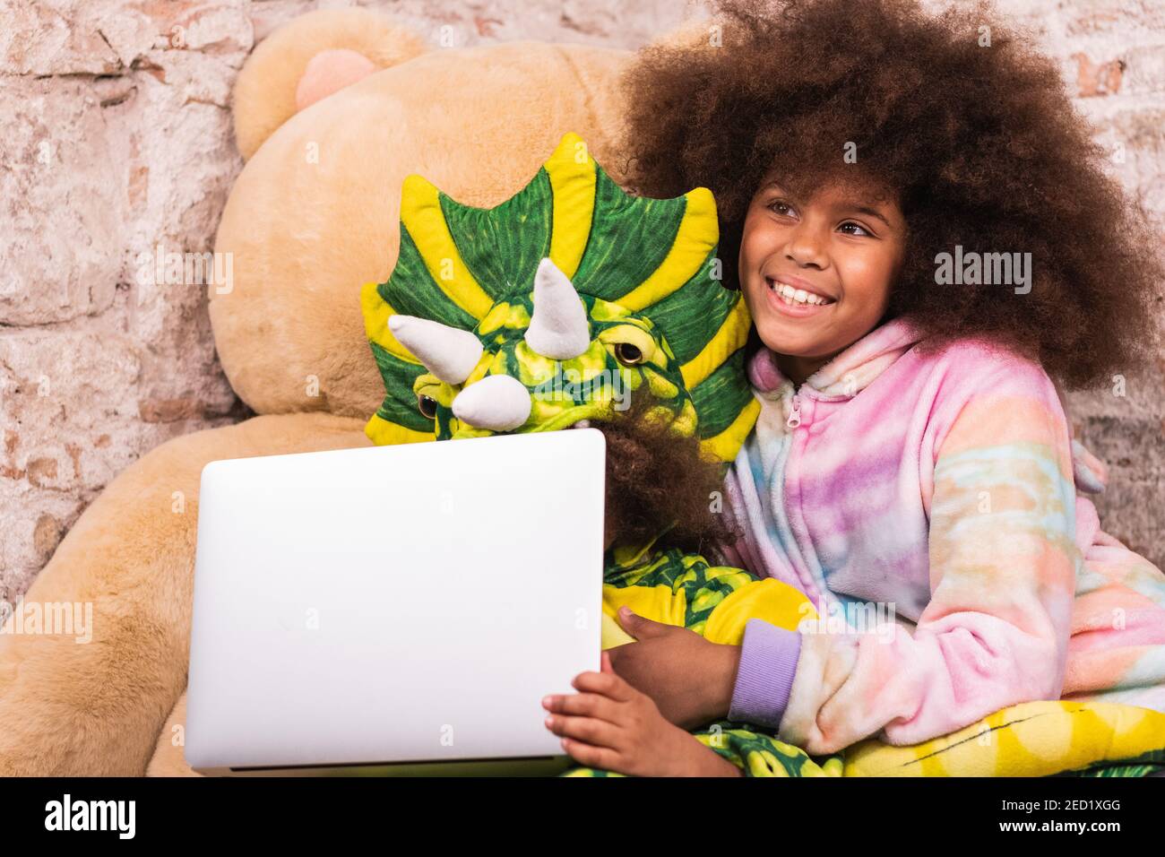 Fratelli positivi in costumi unicorno e drago abbracciando e navigando computer portatile in sala giochi Foto Stock
