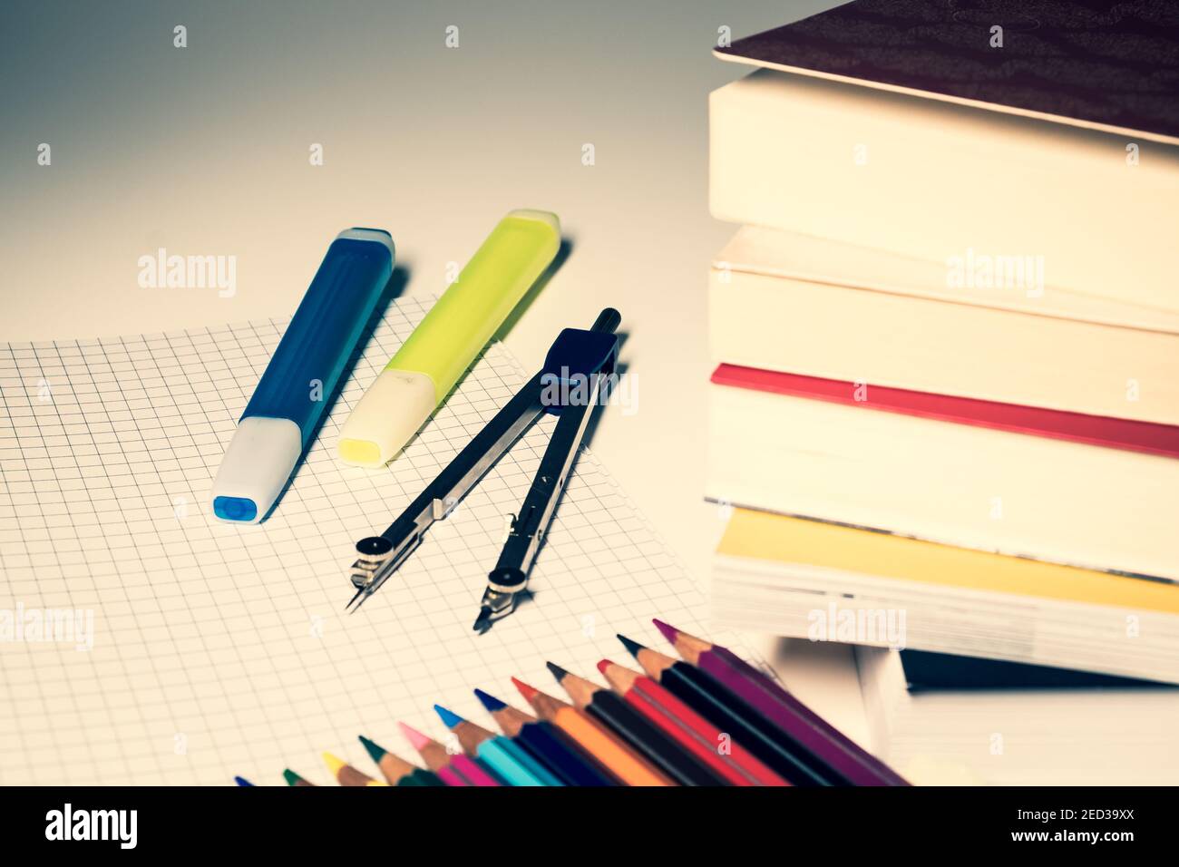 Due evidenziatori e una bussola sono posti su un foglio quadrato, in primo piano una pila di libri e pastelli colorati. Foto Stock