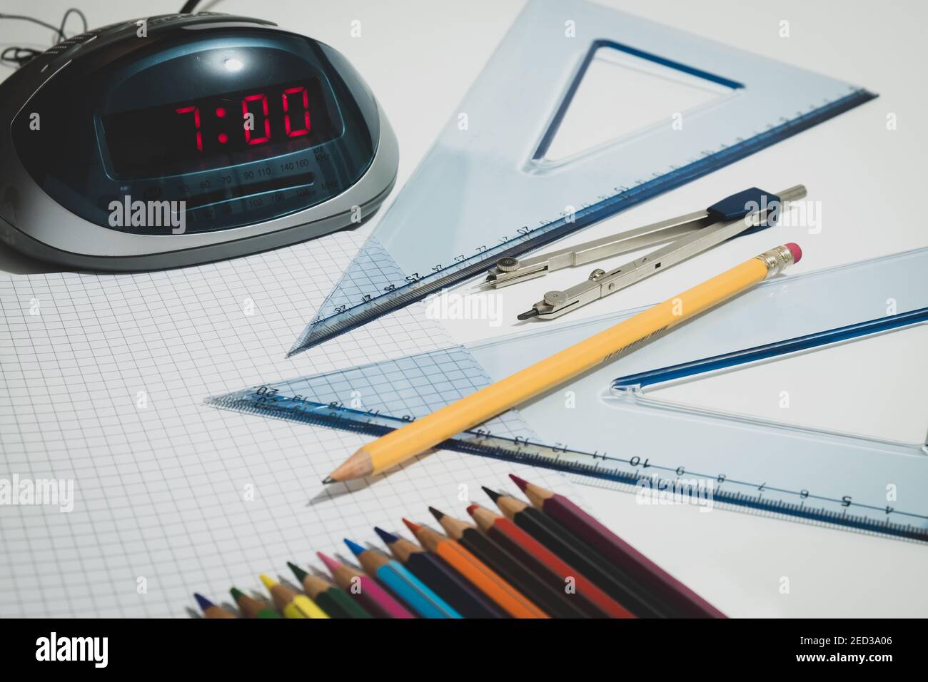 Una sveglia indica le 7 per andare a scuola, una bussola, una matita e tavole da disegno sono collocati nelle vicinanze. Foto Stock