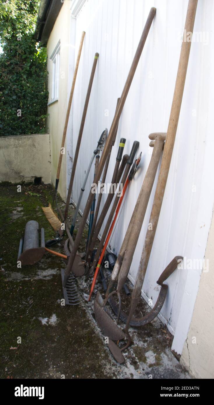 Vecchi attrezzi manuali da giardino appoggiati su una porta del garage. Foto Stock
