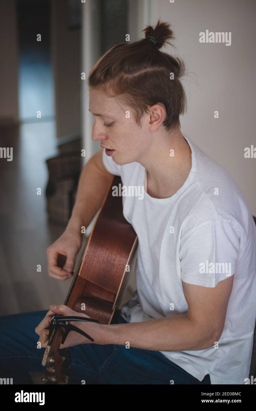 Un ragazzo biondo dall'aspetto casual con i freckles passa il tempo libero a suonare la sua chitarra memoriale e a cantare una canzone d'amore. Classe musicale. Pratica accordi durante Foto Stock
