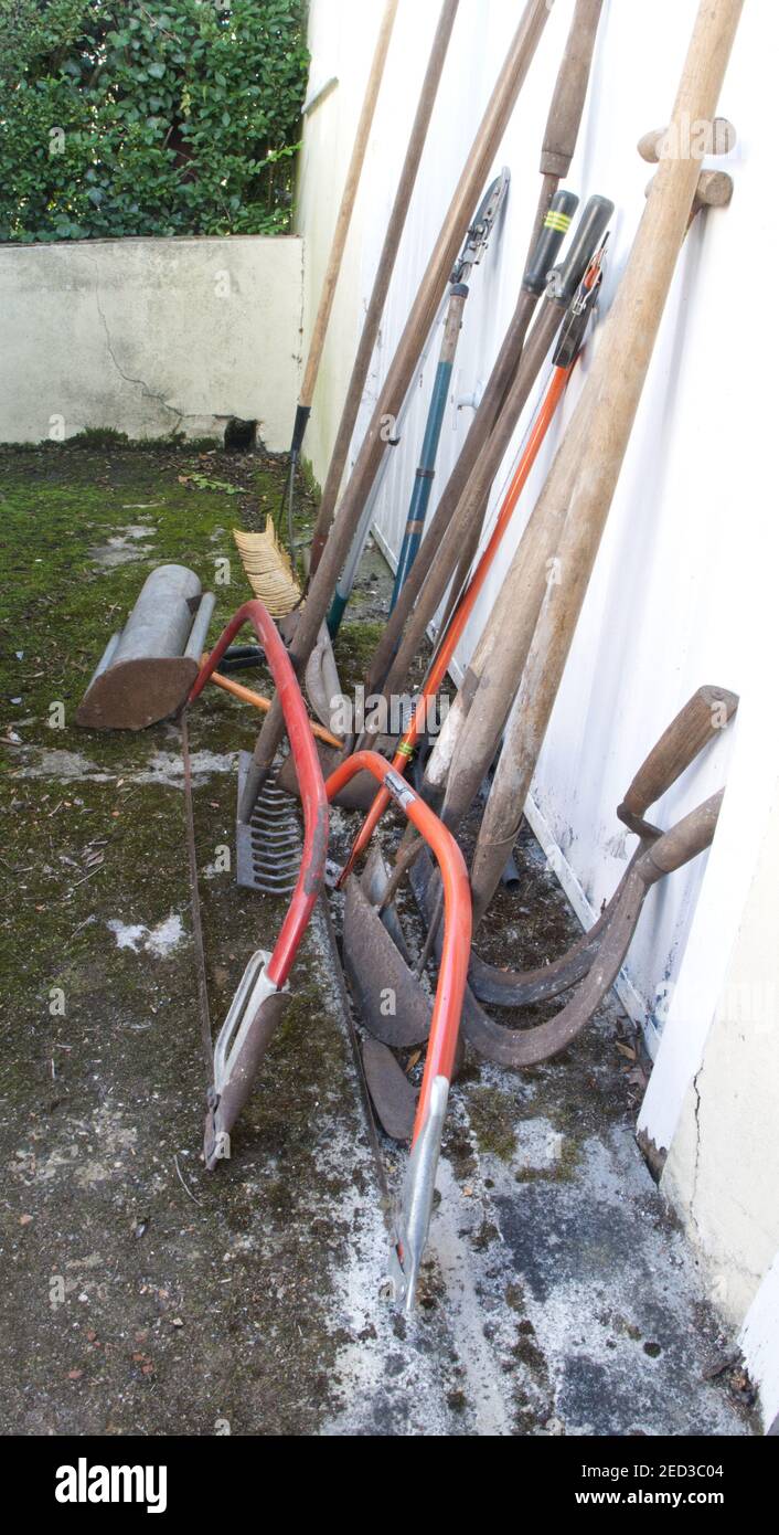 Vecchi attrezzi manuali da giardino appoggiati su una porta del garage. Foto Stock