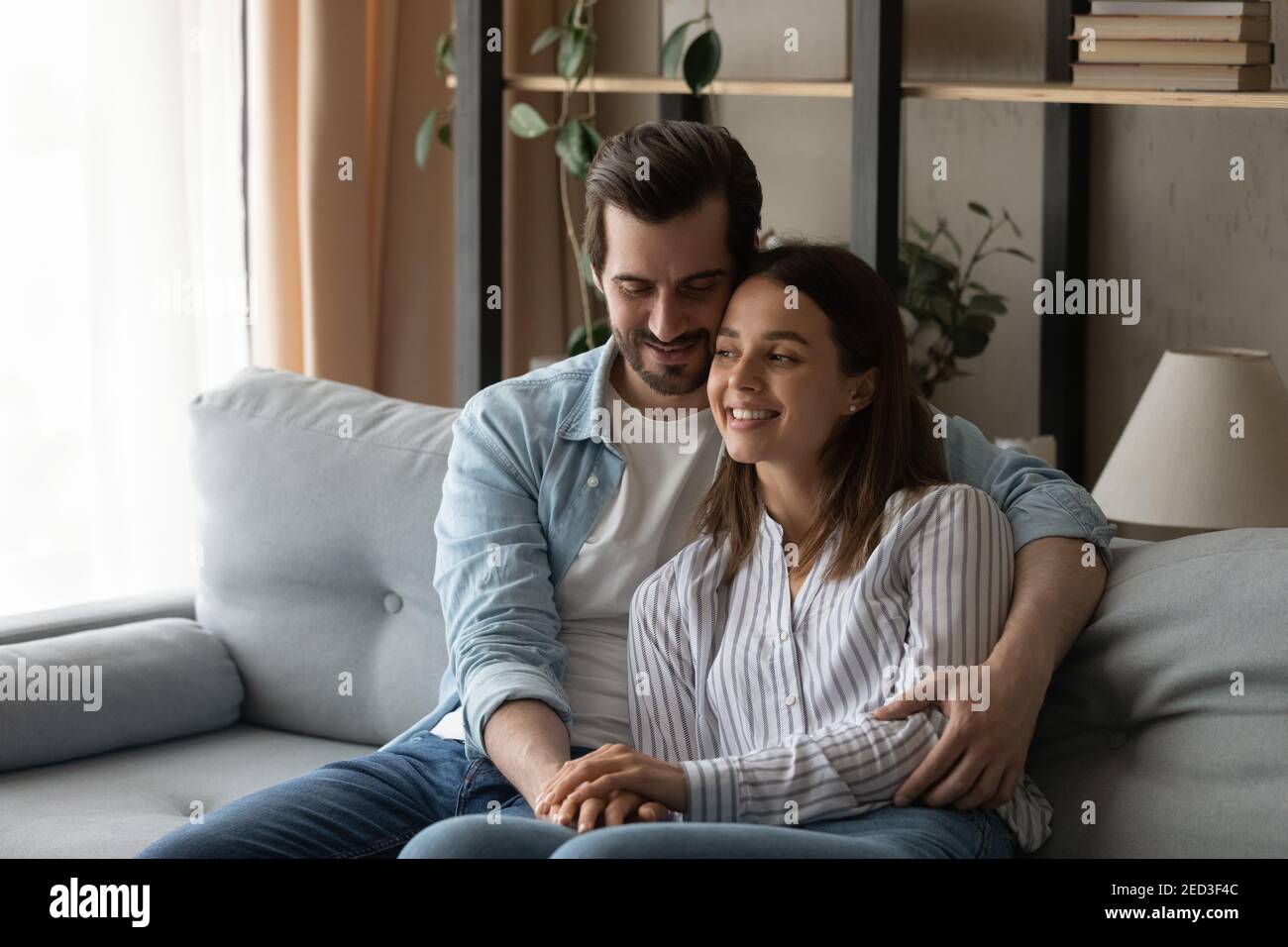 Il giovane marito siede sul divano tenga la moglie amata nelle braccia Foto Stock