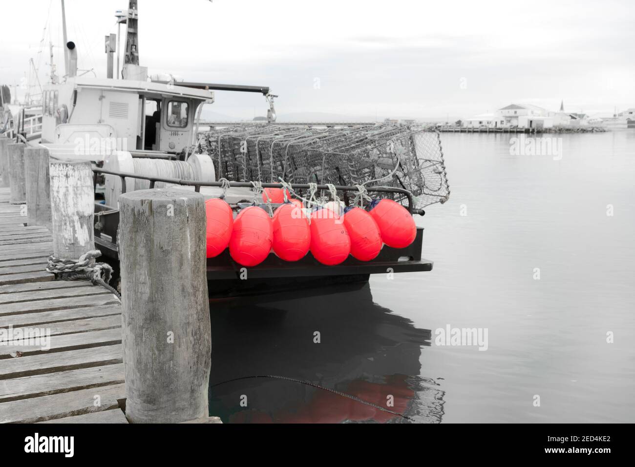 Immagine industriale monocromatica con spot color Barca da pesca con boe rosa brillante legate alla ferrovia di poppa al molo di Riverton South Island Nuova Zelanda. Foto Stock