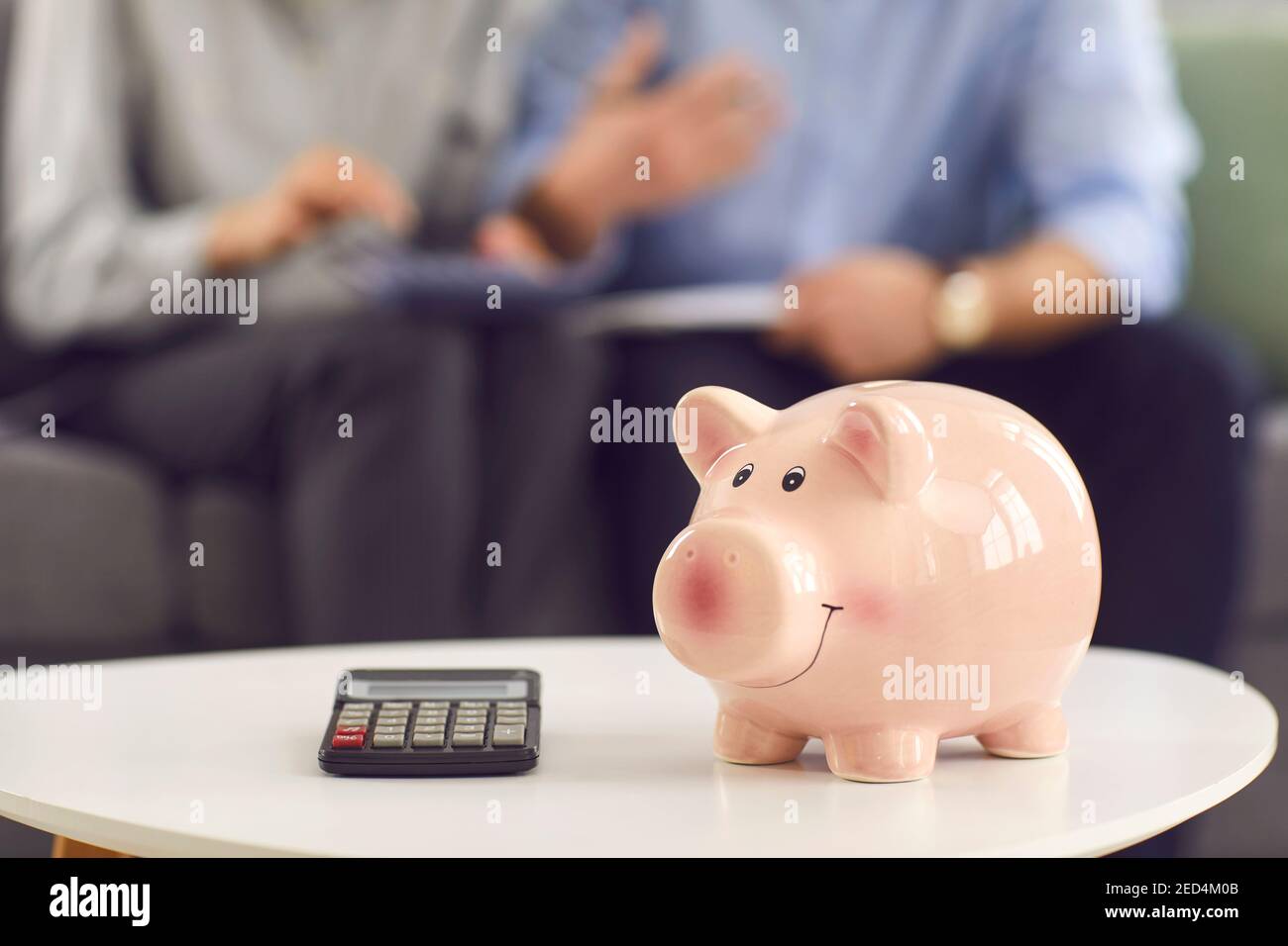 Closeup di banca piggy e calcolatrice sul tavolo, coppia che gestisce il budget di famiglia in background Foto Stock