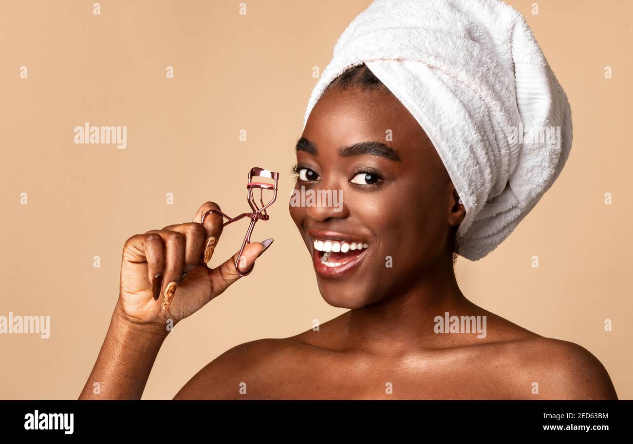 Ritratto di sorridente afroamericano modello femminile utilizzando Eyelash Curler Foto Stock