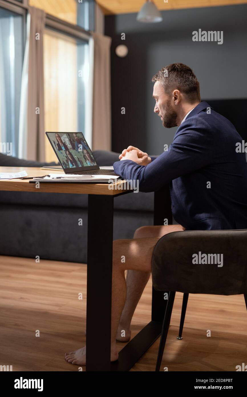 Giovane uomo d'affari contemporaneo con giacca blu scuro e mutande sedute  in poltrona da tavolo davanti al computer portatile durante il video  conferenza Foto stock - Alamy