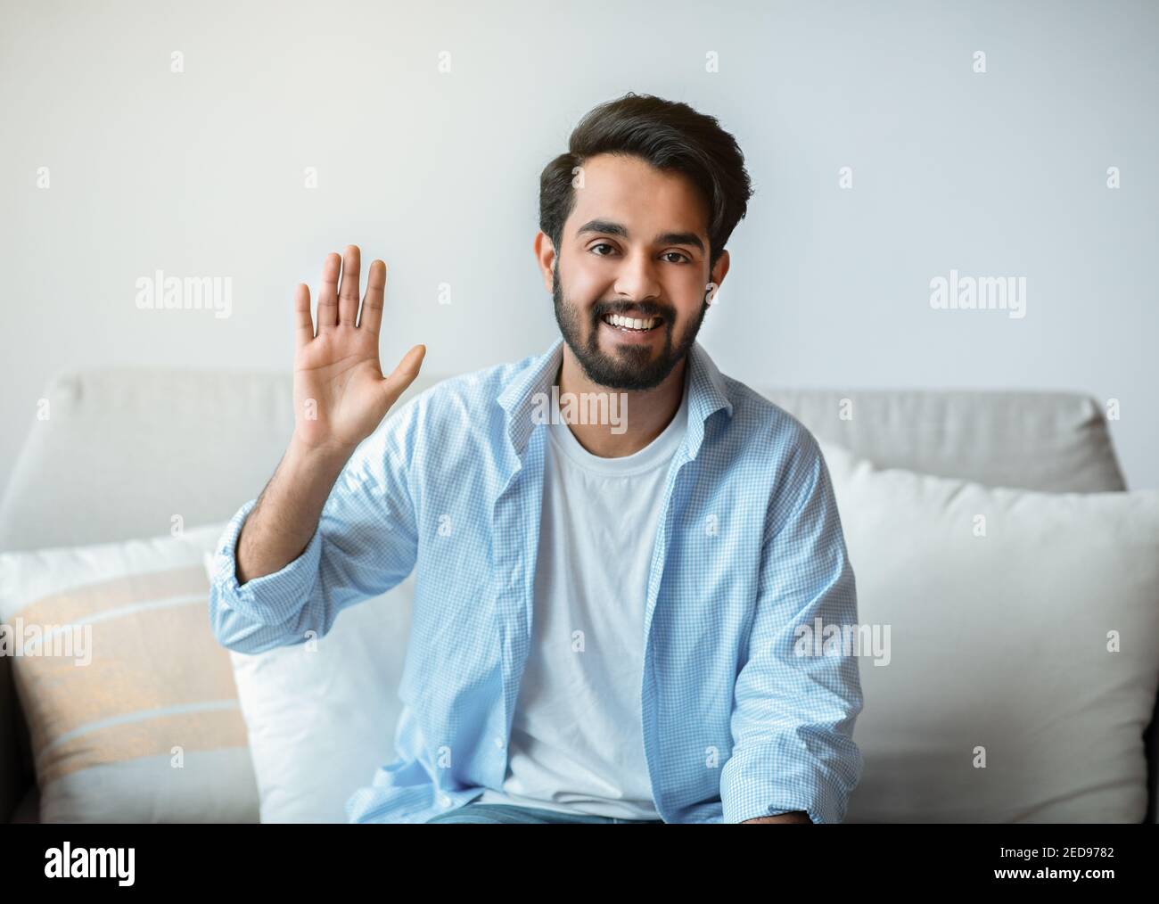 Saluto. Amico uomo orientale che si fa ciao mentre si siede sul divano a casa Foto Stock