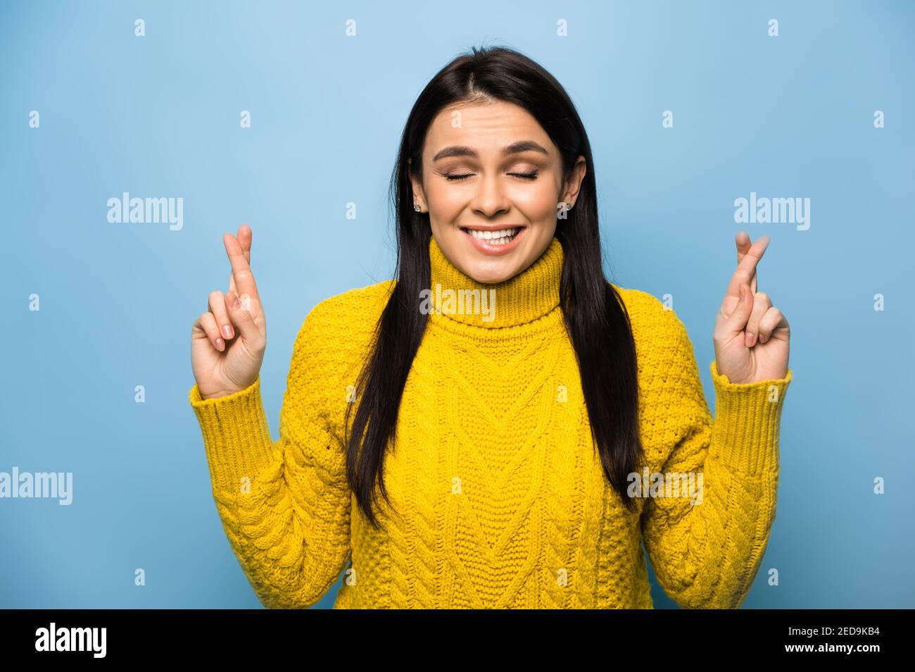 Foto di ragazza caucasica ansiosa sentirsi nervosa circa il suo lavoro di sogno, esame, o vacanza, croce dita morso labbra e occhi chiusi, si trova su sfondo blu isolato. Foto Stock