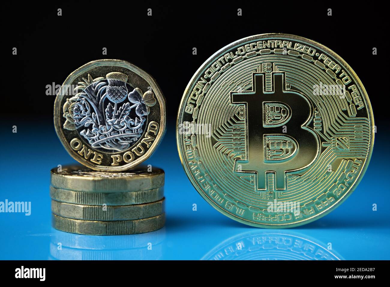 Monete di Bitcoin e British da una libbra messe insieme sulla superficie riflettente con sfondo sfocato. Concetto di criptovaluta rispetto alla curra tradizionale Foto Stock