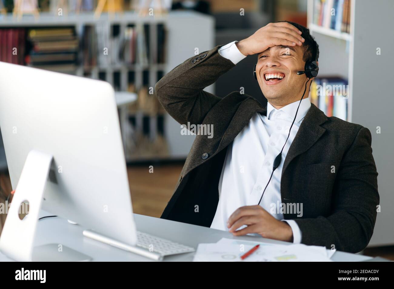 Sorridente business leader, manager o tutor ispanico di successo seduto al tavolo da lavoro con cuffie e sorridente durante una videoconferenza con colleghi o studenti Foto Stock