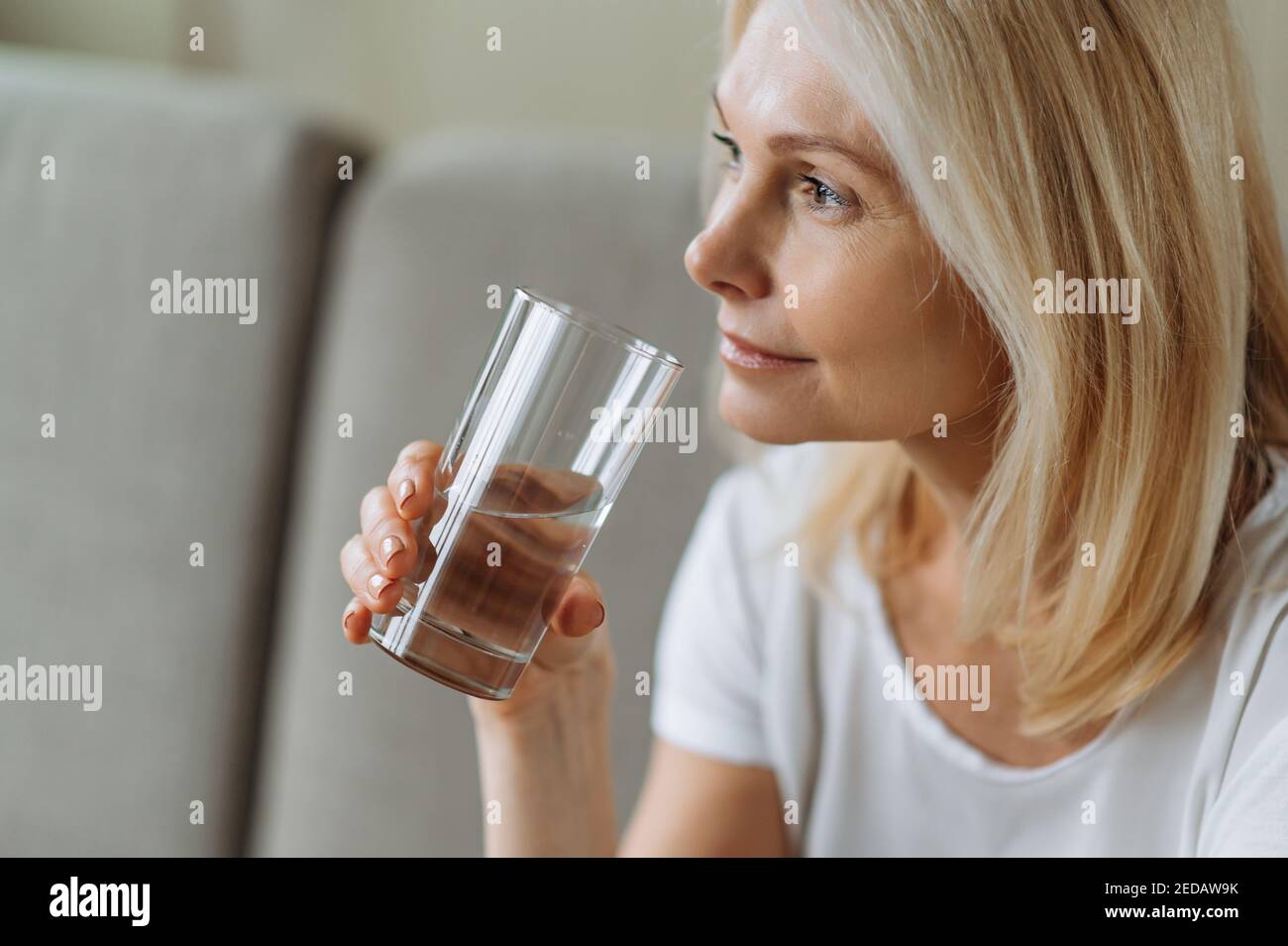 Seguire uno stile di vita sano. Essere sani. Matura bella donna caucasica che tiene un bicchiere di acqua pulita, prendersi cura della sua salute, la norma quotidiana dell'acqua Foto Stock