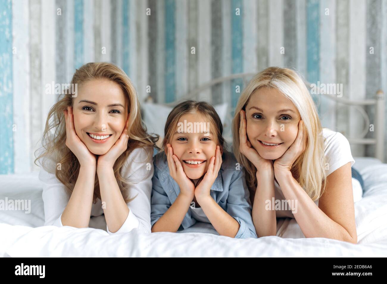 Ritratto di tre generazioni femminili. Nonna, figlia e nipote caucasiche felici si trovano a casa sul divano, guardando la macchina fotografica e sorridendo. Rapporti e valori familiari Foto Stock