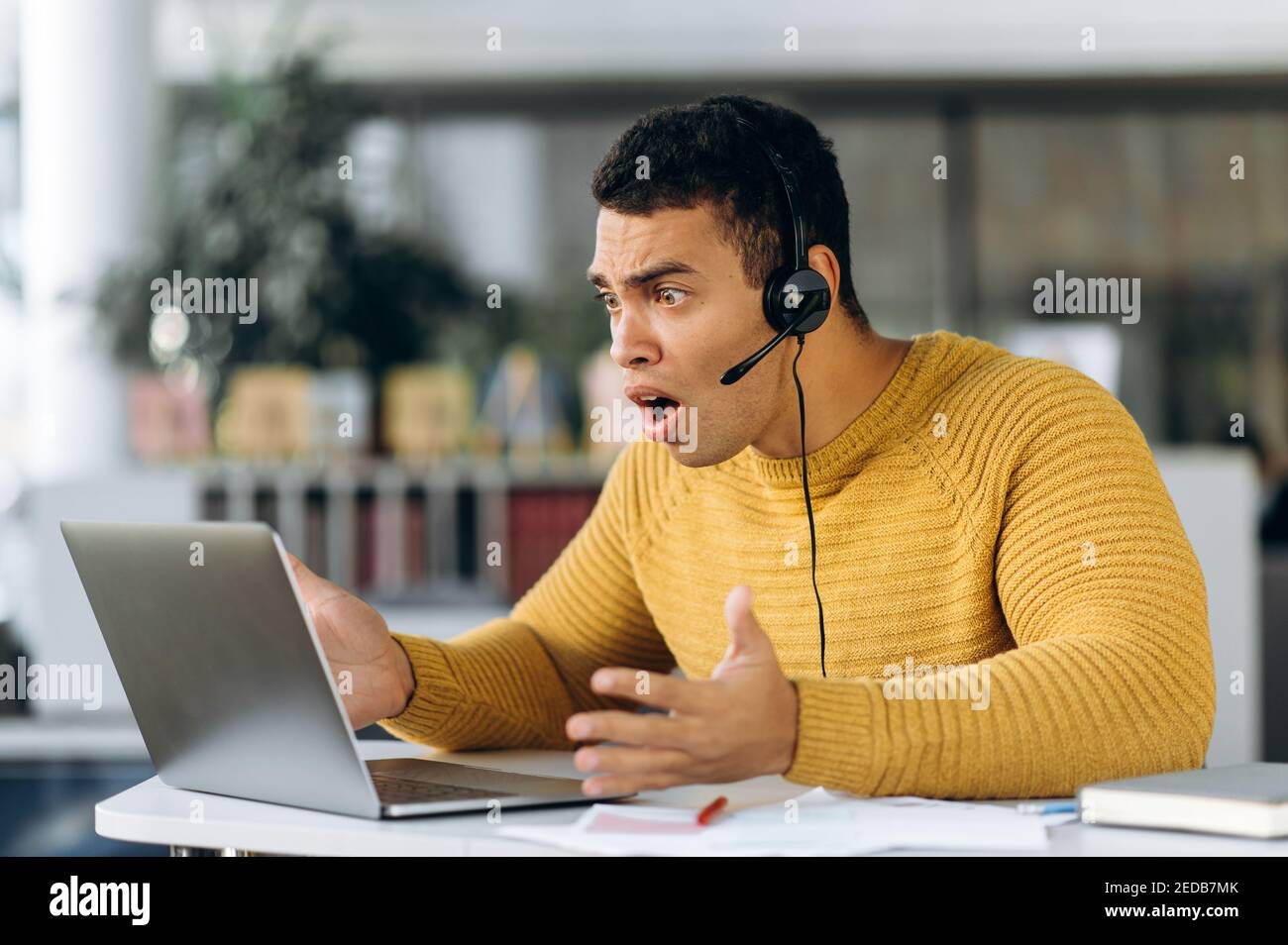 Attraente studente ispanico giovane uomo o collaboratore sorprende guarda computer portatile mentre si lavora o si studia online Foto Stock