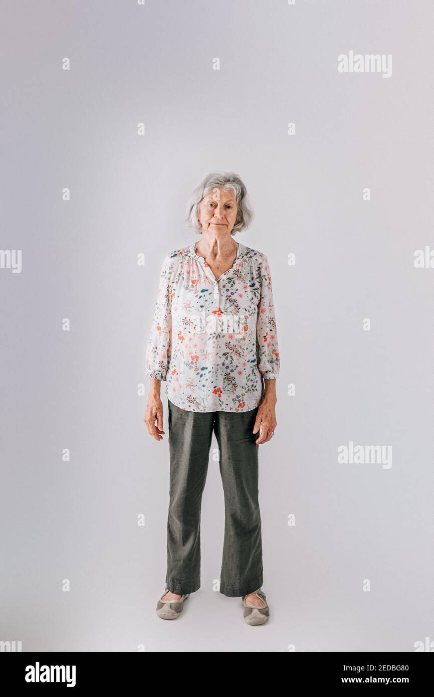 Donna anziana nei suoi anni 80 con capelli grigi in piedi isolati su uno sfondo bianco Foto Stock