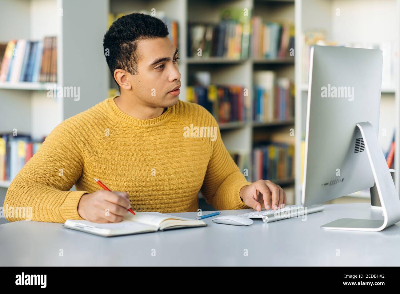 Persona di affari concentrata che lavora in linea. Ispanica maschile freelance idee di ricerca navigare in internet. I dipendenti concentrati si siedono alla scrivania in ufficio e lavorano in remoto Foto Stock