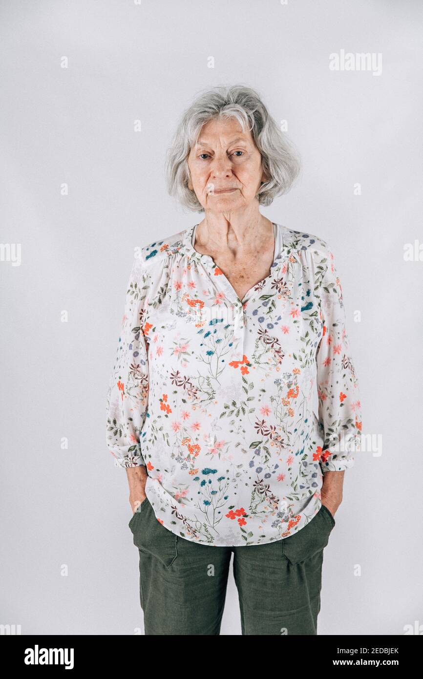 Donna anziana vedova triste negli anni '80 con capelli grigi in piedi isolati su uno sfondo bianco Foto Stock