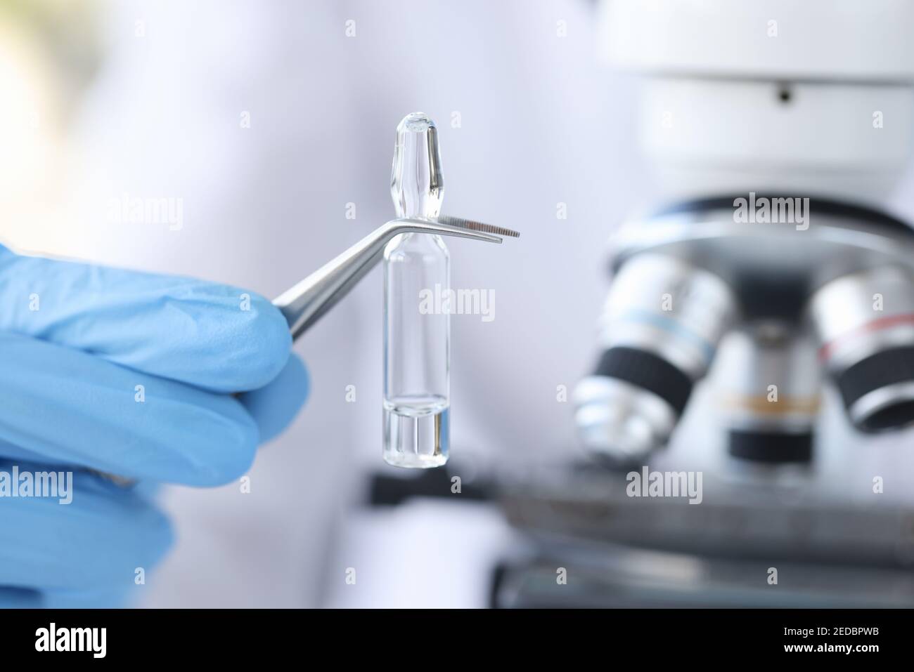 Il guanto a mano contiene il flaconcino con il vaccino contro lo sfondo di microscopio Foto Stock