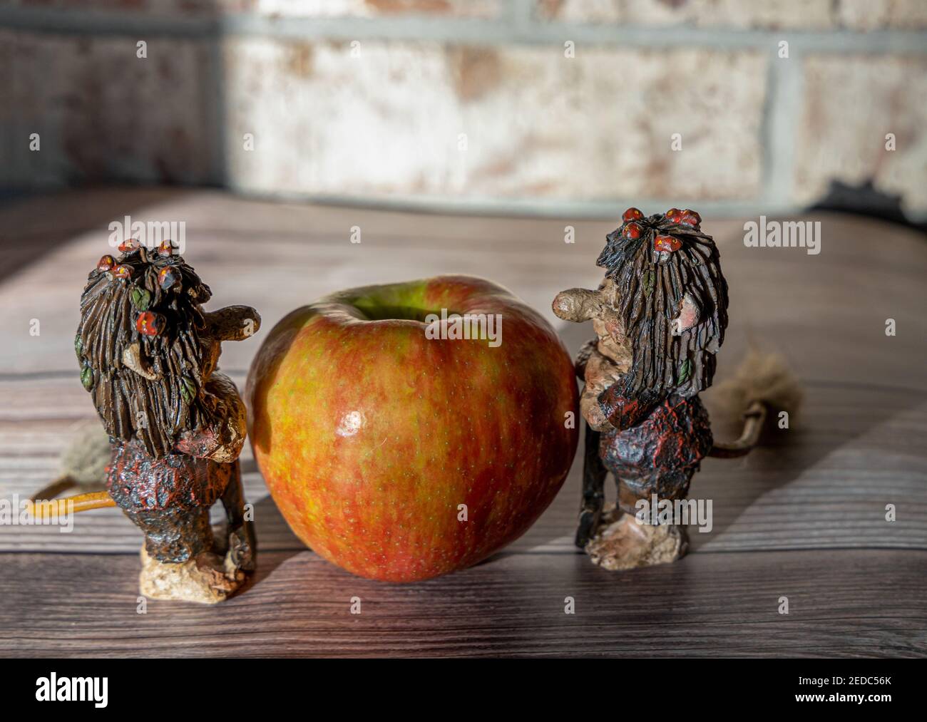 Grandi mele rosse e divertenti troll figure sul legno tavolo contro il muro di mattoni Foto Stock