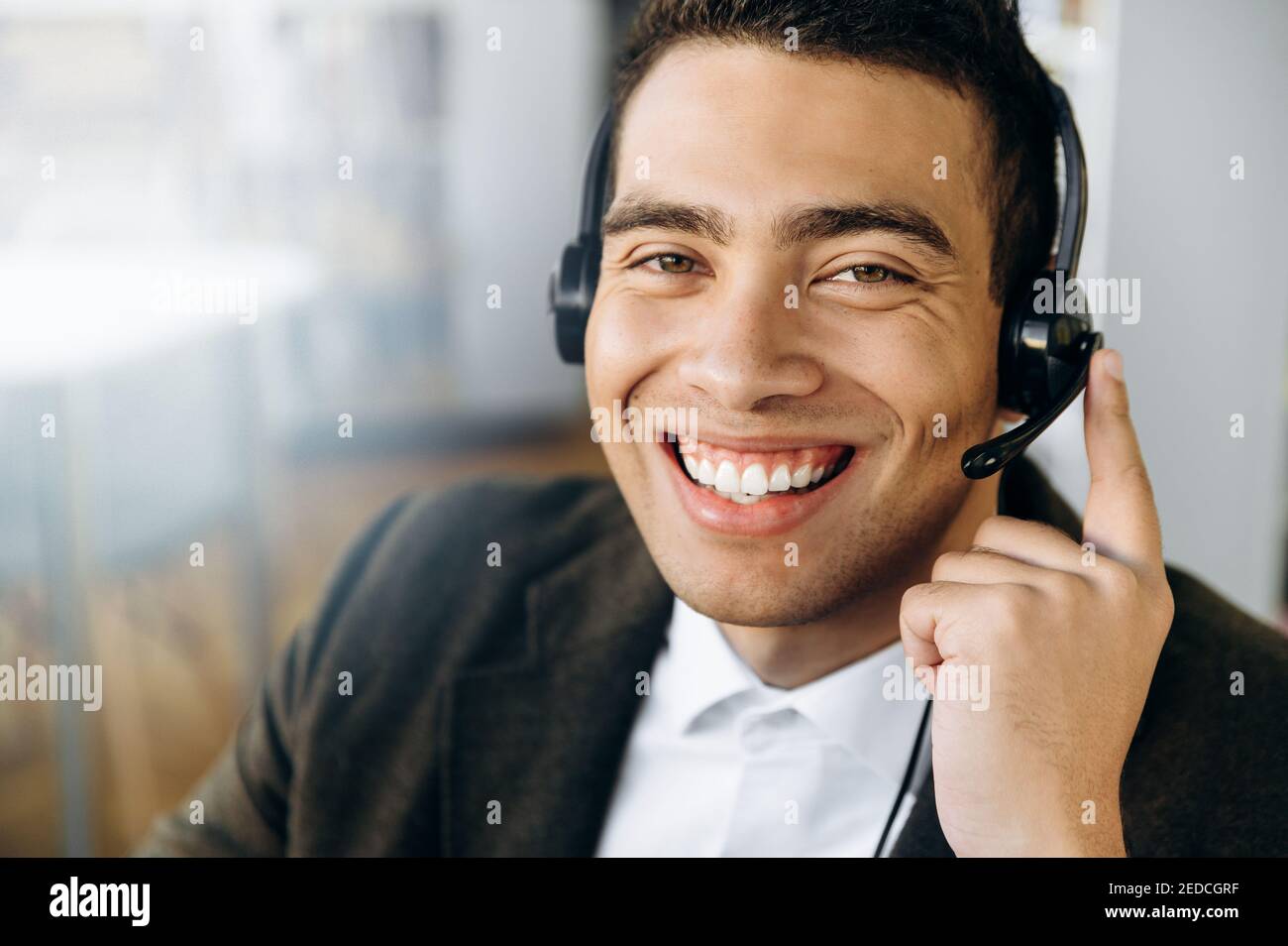 Ritratto dell'operatore ispanico del call center. Consulente maschile soddisfatto seduto alla scrivania, indossando la cuffia guarda direttamente la fotocamera con un sorriso amichevole Foto Stock