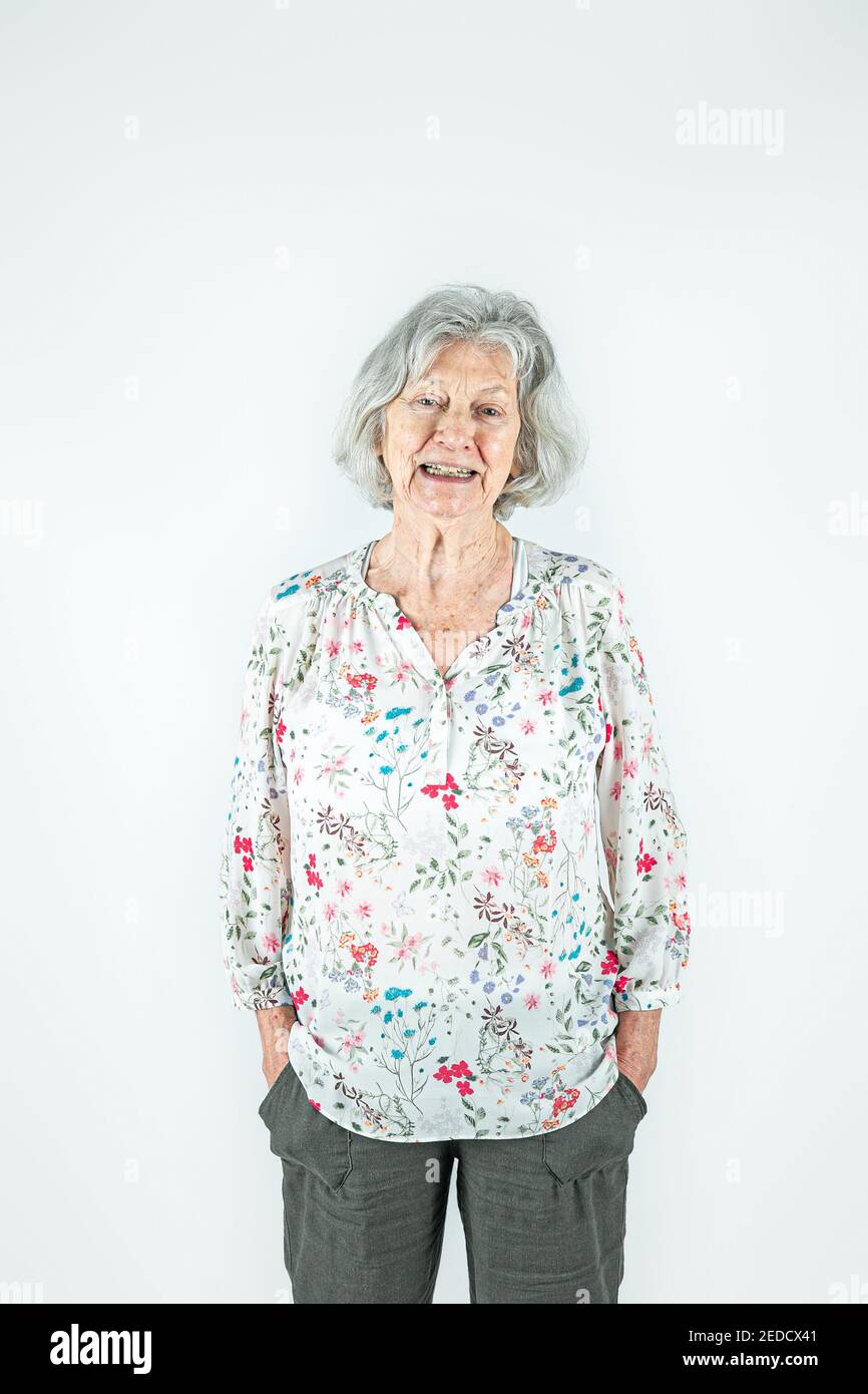 Donna anziana felice nei suoi anni '80 con capelli grigi in piedi isolato su uno sfondo bianco Foto Stock